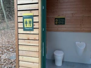 Auf dem Foto ist eine Nahaufnahme des Toilettenraums. Man erkennt deutlich den Toilettenstuhl sowie das Urinal.
