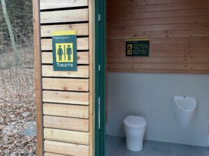 Auf dem Foto ist eine Nahaufnahme des Toilettenraums. Man erkennt deutlich den Toilettenstuhl sowie das Urinal.